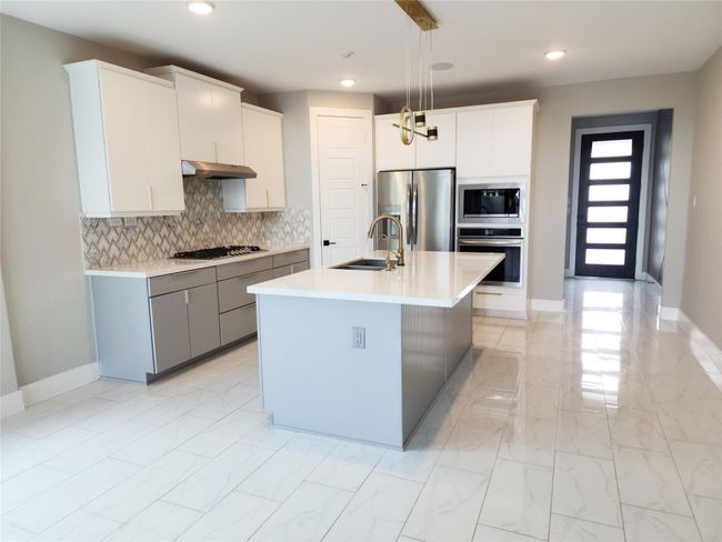 The floors are a beautiful upgrade on this home, the sleek polished tile curated to accommodate the modern style and complemented by the upgrade of the backsplash and the two tones cabinets made this area an instant appeal for the chef of the family. | Image 7