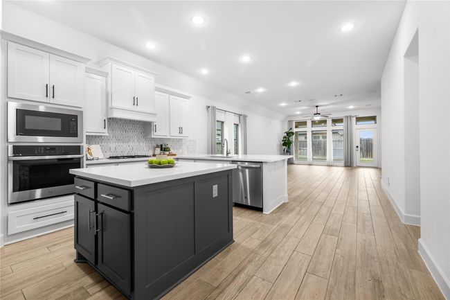 A spacious, modern kitchen with white cabinetry, a large island, stainless steel appliances, and a stylish backsplash. | Image 7