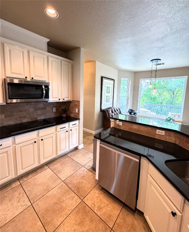 Kitchen featuring dark countertops, stainless steel appliances, hanging light fixtures, tasteful backsplash, and a textured ceiling. | Image 10