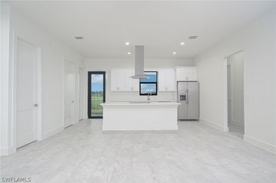 Kitchen with stainless steel refrigerator with ice dispenser, island range hood, white cabinetry, a center island, and light tile floors | Image 2