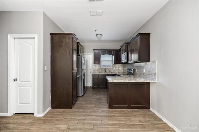Kitchen with stainless steel appliances, dark brown cabinets, a peninsula, light wood finished floors, and decorative backsplash | Image 4