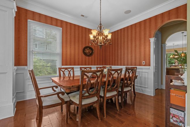 Dining space featuring arched walkways, a chandelier, wainscoting, wood-type flooring, and a decorative wall | Image 11