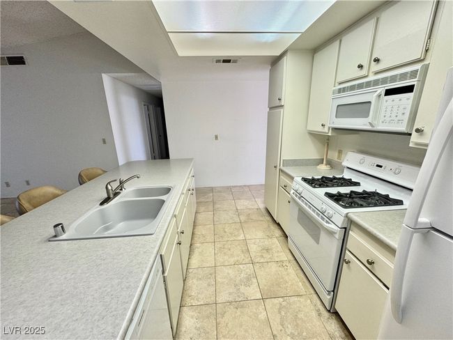 Kitchen featuring white appliances, a sink, light countertops, and white cabinets | Image 4