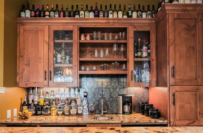Bar in Den featuring wet bar, ice maker, fridge, wine fridge, sink, storage for bottles glassware, and tasteful backsplash | Image 7