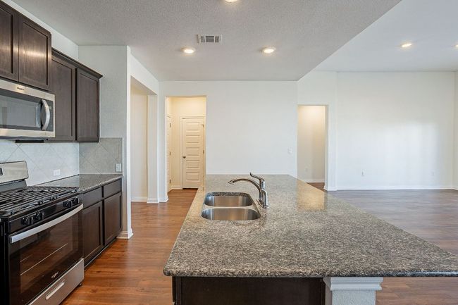 Kitchen featuring a sink, tasteful backsplash, appliances with stainless steel finishes, a kitchen island with sink, and visible vents | Image 6