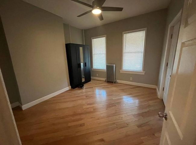 Unfurnished bedroom with radiator, a ceiling fan, light wood-style flooring, and baseboards | Image 4