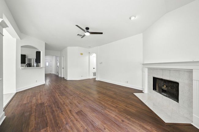 Living room with lofted ceiling, a ceiling fan, a tile fireplace, wood finished floors, and arched walkways | Image 8