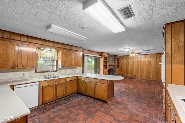 Kitchen with dishwasher, a sink, brown cabinets, light countertops, and wooden walls | Image 14