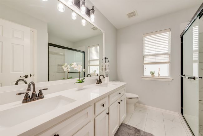 Bathroom with a shower stall, double vanity, marble look tiles, toilet, and baseboards | Image 27