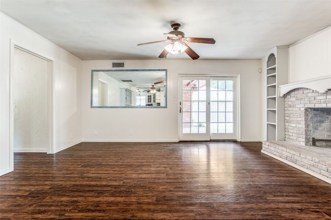 Unfurnished living room featuring ceiling fan, wood finished floors, a brick fireplace, baseboards, and built in features | Image 22