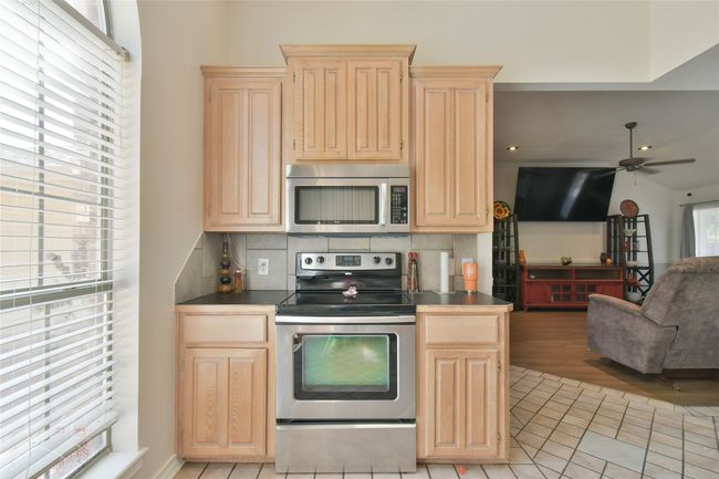 Kitchen with stainless steel appliances, light brown cabinetry, tasteful backsplash, a ceiling fan, and light tile patterned flooring | Image 36