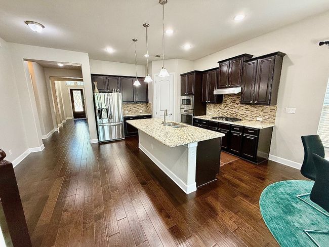 Kitchen featuring appliances with stainless steel finishes, backsplash, a sink, under cabinet range hood, and dark wood-type flooring | Image 4