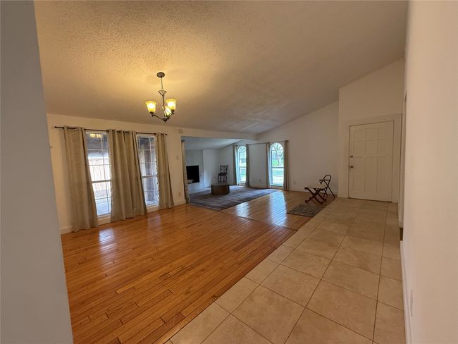Unfurnished living room with a chandelier, a textured ceiling, light wood-style flooring, and lofted ceiling | Image 4