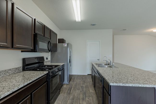 Kitchen with black appliances, a sink, dark wood-style floors, dark brown cabinets, and an island with sink | Image 7