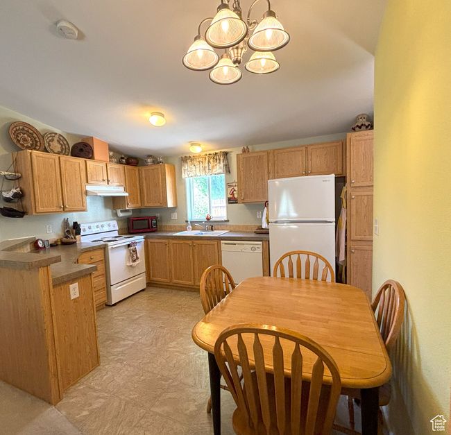 Kitchen featuring white appliances, a chandelier, under cabinet range hood, a sink, and dark countertops | Image 23