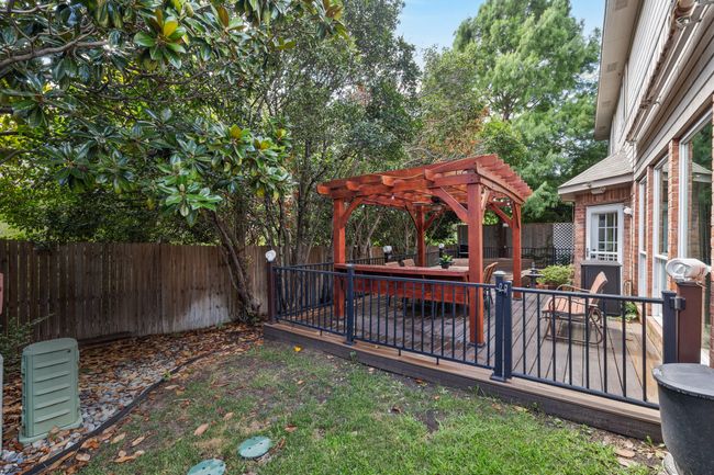 Fenced backyard featuring a pergola, synthetic wood deck with seating area, planter boxes and grassy areas on each side. | Image 37