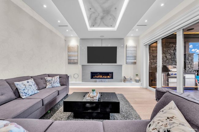 Living area featuring a glass covered fireplace, wood finished floors, recessed lighting, and a raised ceiling | Image 29