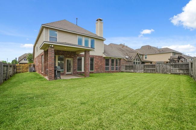 Spacious backyard featuring a well-maintained lawn and a two-story brick house with a covered patio, perfect for outdoor activities and entertaining. | Image 35