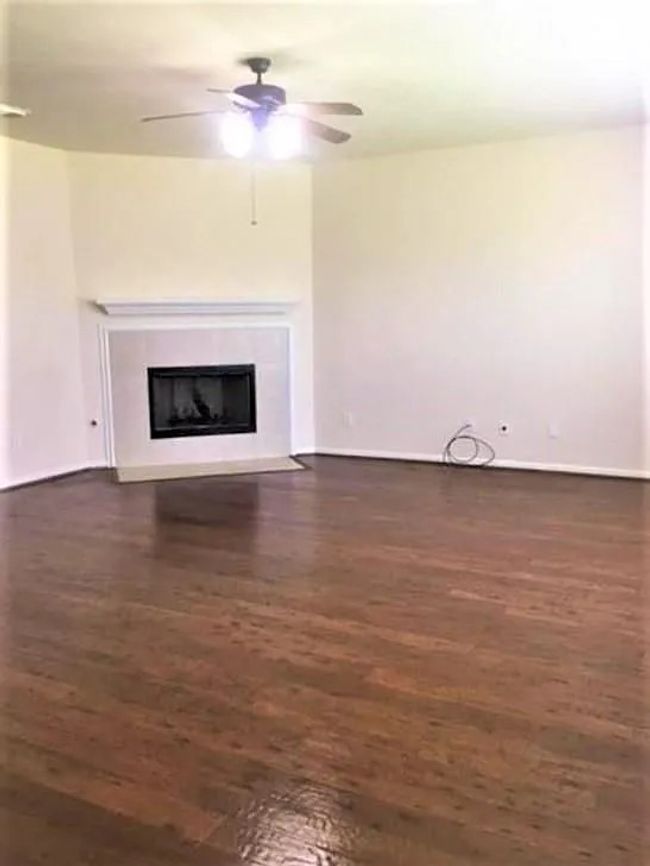 Unfurnished living room with ceiling fan, dark wood finished floors, a fireplace with flush hearth, and baseboards | Image 7