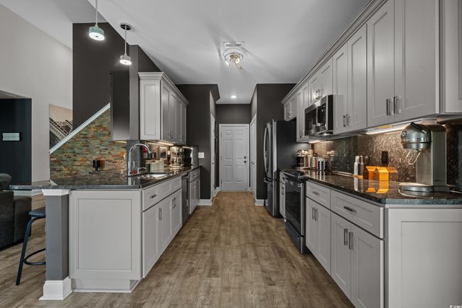 Kitchen featuring appliances with stainless steel finishes, a breakfast bar area, tasteful backsplash, wood finished floors, and dark stone counters | Image 14