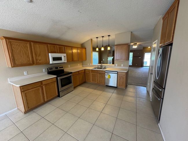 Kitchen with stainless steel appliances, light tile patterned floors, a textured ceiling, light countertops, and brown cabinetry | Image 4