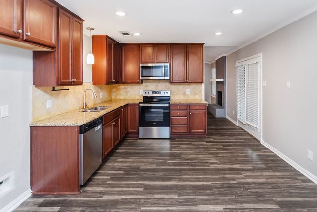 Kitchen featuring stainless steel appliances, dark wood-style floors, light stone counters, backsplash, and crown molding | Image 7