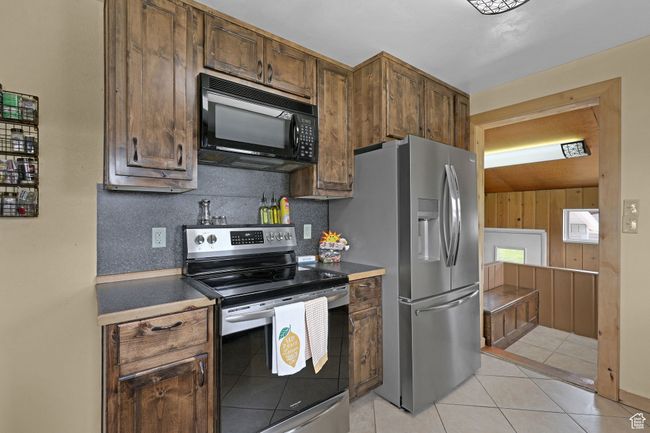 Kitchen with stainless steel appliances, light tile patterned floors, dark countertops, and tasteful backsplash | Image 13