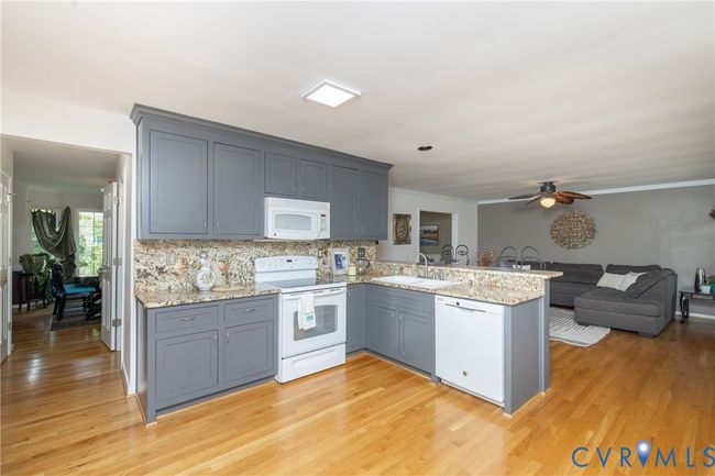 Kitchen with a peninsula, white appliances, a ceiling fan, tasteful backsplash, and light wood-type flooring | Image 13
