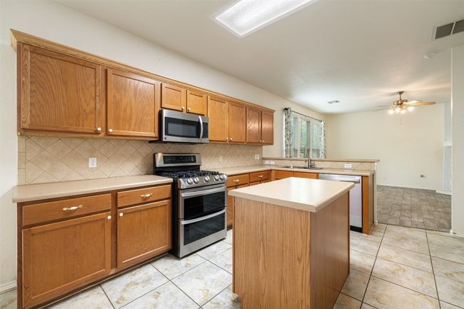 Kitchen featuring visible vents, decorative backsplash, a peninsula, a sink, and appliances with stainless steel finishes | Image 10