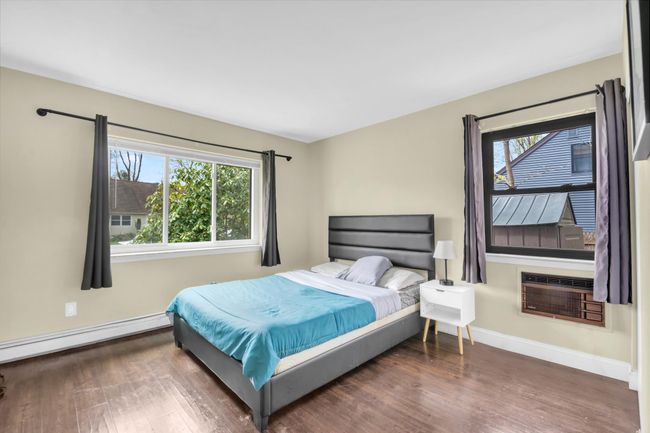 Bedroom featuring a baseboard radiator, a wall mounted air conditioner, wood finished floors, and multiple windows | Image 19
