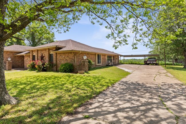 Ranch-style home featuring brick siding, a shingled roof, a front yard, and a carport | Image 6