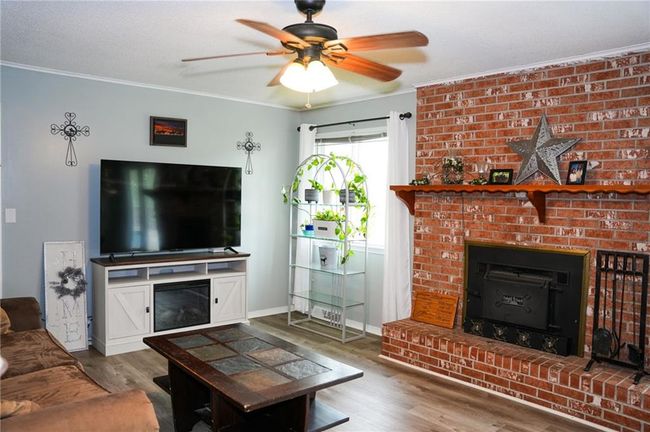 Living area with wood finished floors, ceiling fan, a brick fireplace, baseboards, and crown molding | Image 8