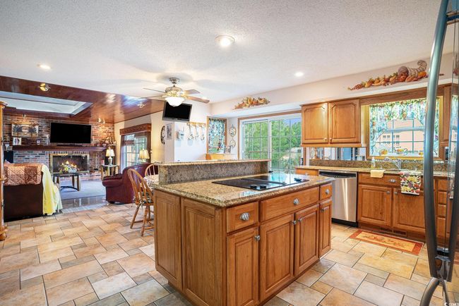 Kitchen with stainless steel dishwasher, black electric cooktop, ceiling fan, a textured ceiling, and a kitchen island | Image 10
