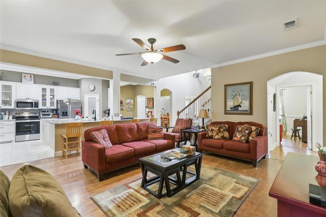 Living area with arched walkways, a ceiling fan, ornamental molding, stairs, and light wood finished floors | Image 17