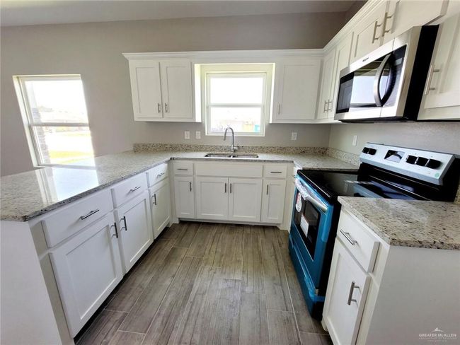 Kitchen with appliances with stainless steel finishes, a peninsula, wood finished floors, white cabinetry, and light stone countertops | Image 5