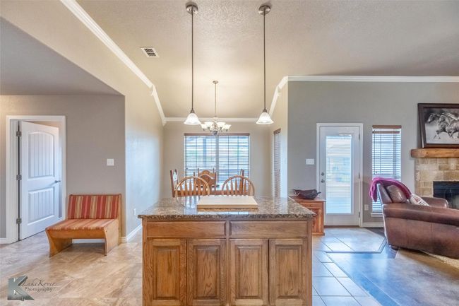 Kitchen with crown molding, a chandelier, light tile patterned floors, stone counters, and open floor plan | Image 10