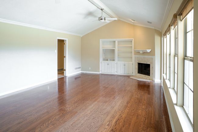 Unfurnished living room with ceiling fan, wood finished floors, a tiled fireplace, and ornamental molding | Image 5