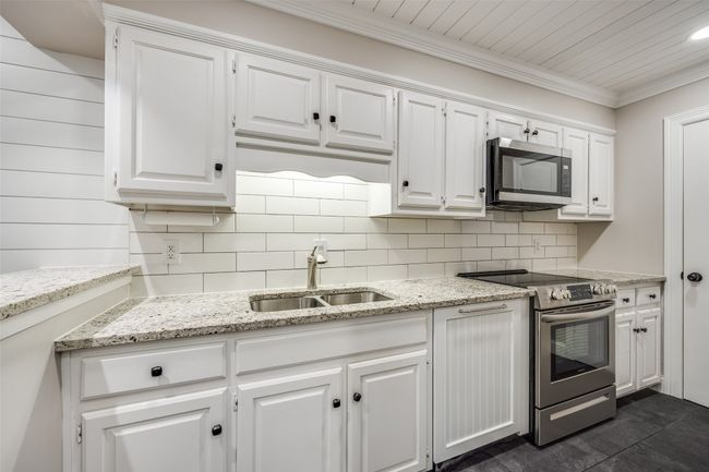 Kitchen featuring appliances with stainless steel finishes, white cabinets, tasteful backsplash, light stone countertops, and ornamental molding | Image 4