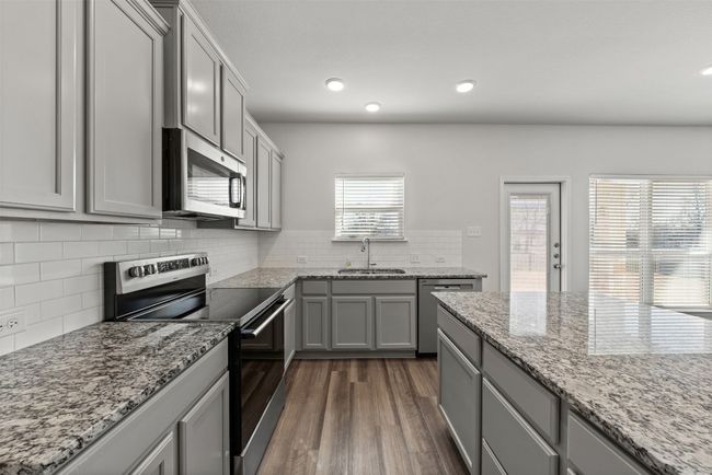 Kitchen with appliances with stainless steel finishes, gray cabinetry, dark wood finished floors, backsplash, and light stone counters | Image 12