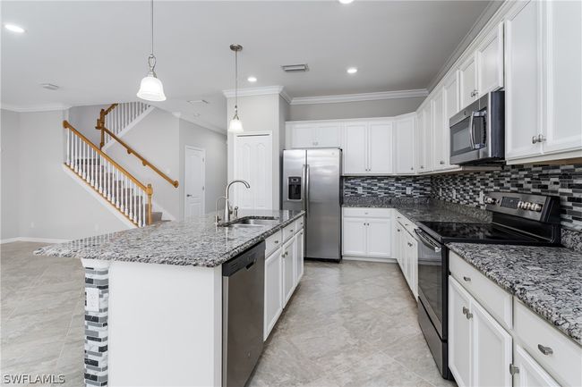 Kitchen with stainless steel appliances, backsplash, light tile floors, and a kitchen island with sink | Image 11