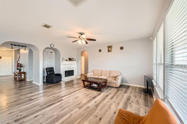 Spacious open concept living room with light wood flooring, a cozy fireplace, and tons of natural light from the large windows. | Image 8