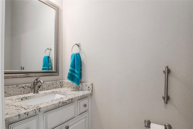 This half bathroom features a sleek granite countertop with a modern sink and faucet. It includes a large mirror, towel ring, and located right off the home office. The space is accented with a grab bar, adding functionality. | Image 23