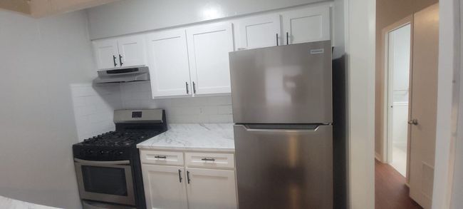 Kitchen with appliances with stainless steel finishes, under cabinet range hood, tasteful backsplash, light stone counters, and white cabinetry | Image 18