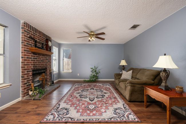 Living area with visible vents, ceiling fan, a brick fireplace, and wood finished floors | Image 13
