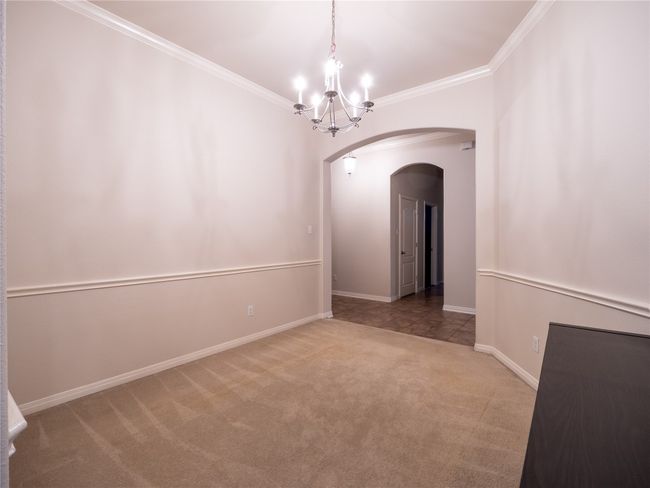 Carpeted dining room (or flex room) with arched walkways, a chandelier, crown molding, and baseboards | Image 4
