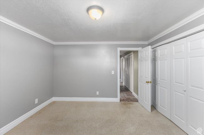 Unfurnished bedroom with a textured ceiling, a closet, ornamental molding, carpet flooring, and baseboards | Image 20