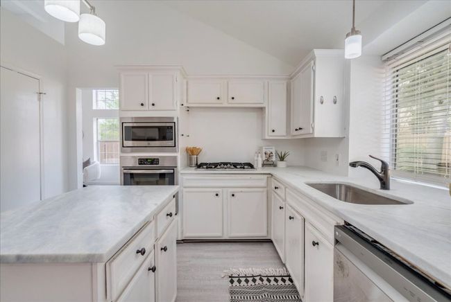 Kitchen with stainless steel appliances, a sink, lofted ceiling, white cabinetry, and decorative light fixtures | Image 10