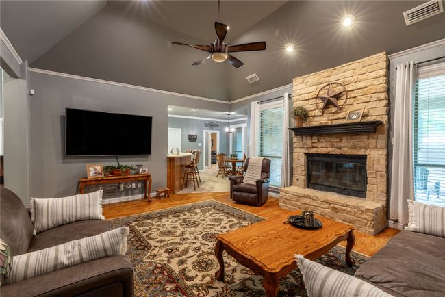 Living area with a ceiling fan, wood finished floors, high vaulted ceiling, and a fireplace | Image 13