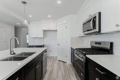 Kitchen with hanging light fixtures, sink, white cabinetry, appliances with stainless steel finishes, and light hardwood / wood-style floors | Image 3