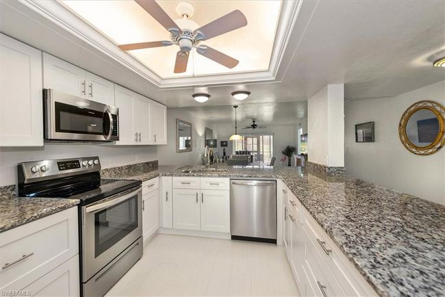 Kitchen featuring stainless steel appliances, a ceiling fan, a raised ceiling, white cabinets, and dark stone counters | Image 9